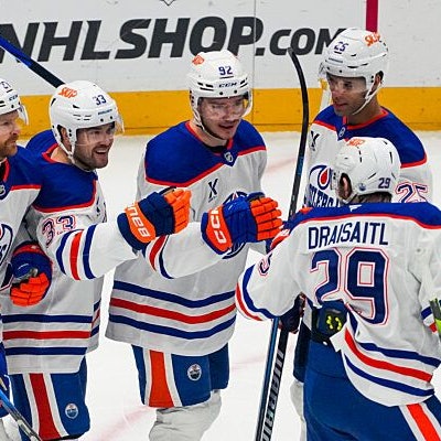 Fünft Eishockeyspieler stehen in ihrem Trikot auf dem Eis und geben sich freudig einen Handschlag.