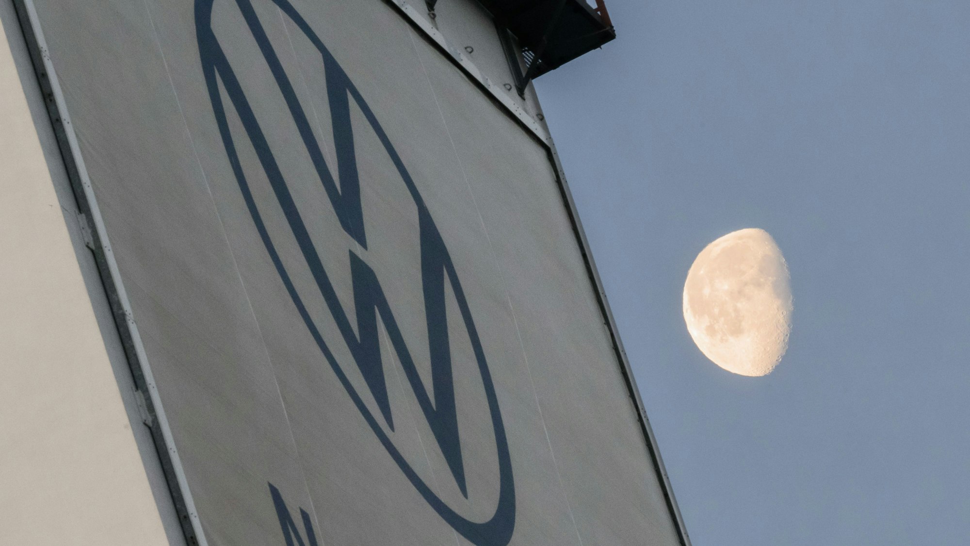 VW verschärft seinen Sparkurs. Das VW-Logo ist an einer Wand zu sehen, im Hintergrund sieht man den Mond.