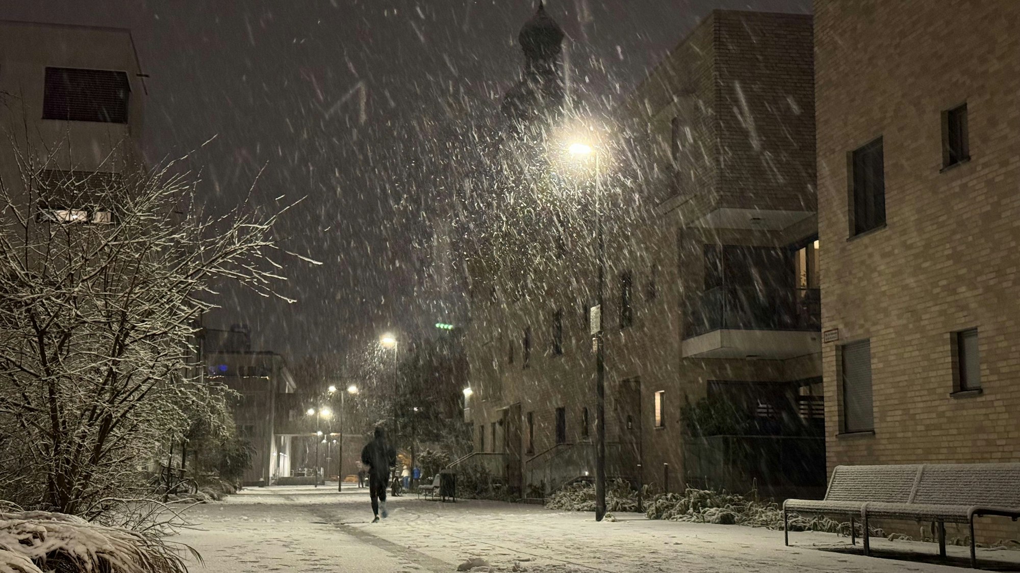08.01.2025, Köln: Vom Schnee bedeckt sind die Straßen im Ortsteil Sülz auf dem Gelände des ehemaligen Kinderheimes mit der Kirche "Zur heiligen Familie". Am Abend hat es in der Stadt begonnen, zu schneien. Foto: Matthias Heinekamp