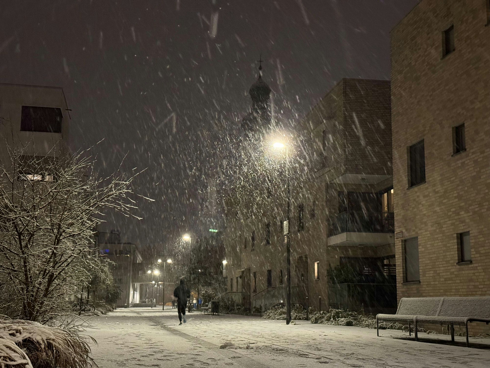 08.01.2025, Köln: Vom Schnee bedeckt sind die Straßen im Ortsteil Sülz auf dem Gelände des ehemaligen Kinderheimes mit der Kirche "Zur heiligen Familie". Am Abend hat es in der Stadt begonnen, zu schneien. Foto: Matthias Heinekamp