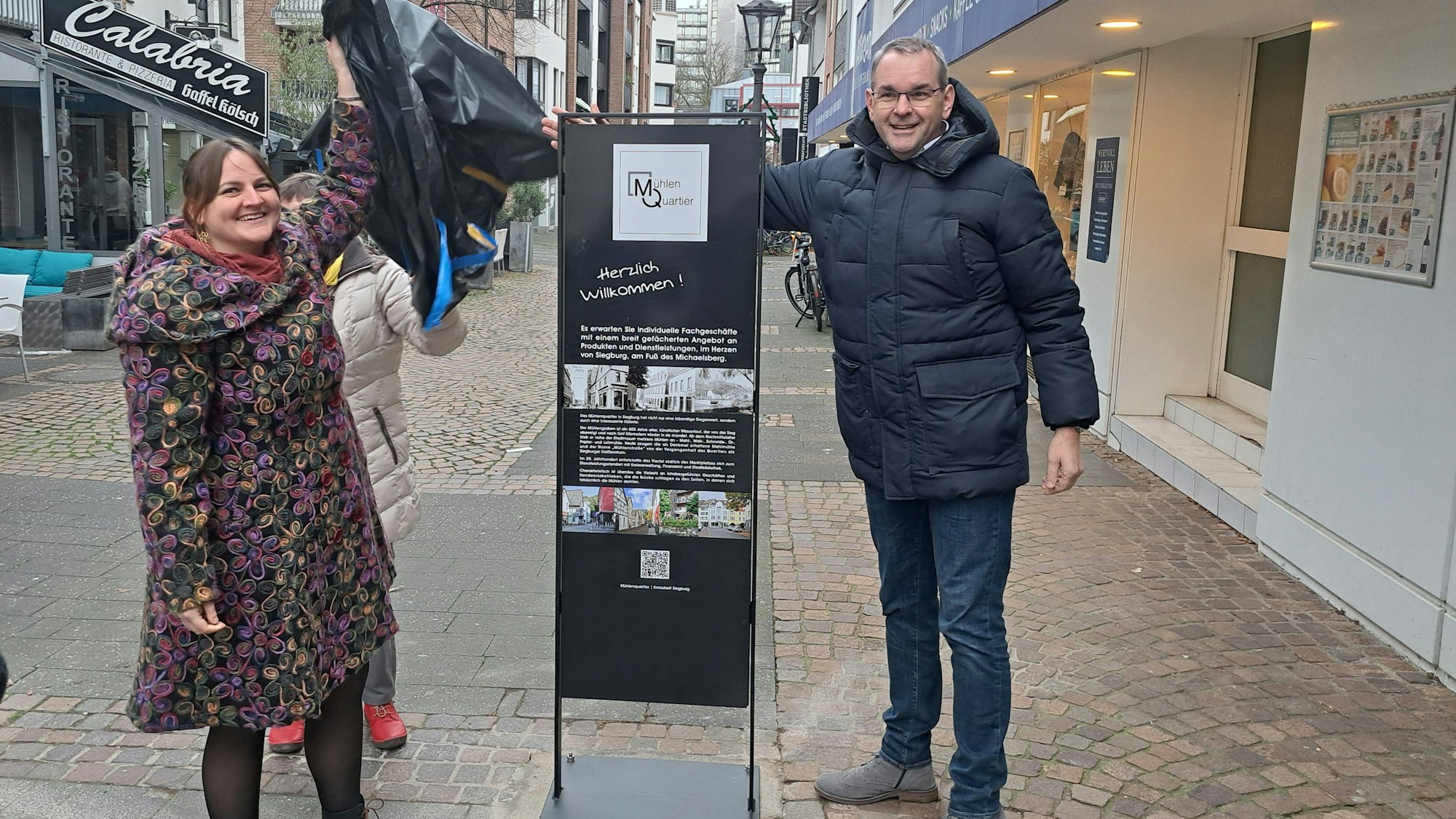 Eine neue Stele lädt jetzt in das Siegburger Mühlenquartier ein. Nadine Weißenfels von der Initiative Mühlenquartier und Bürgermeister Stefan Rosemann enthüllten das Schild.