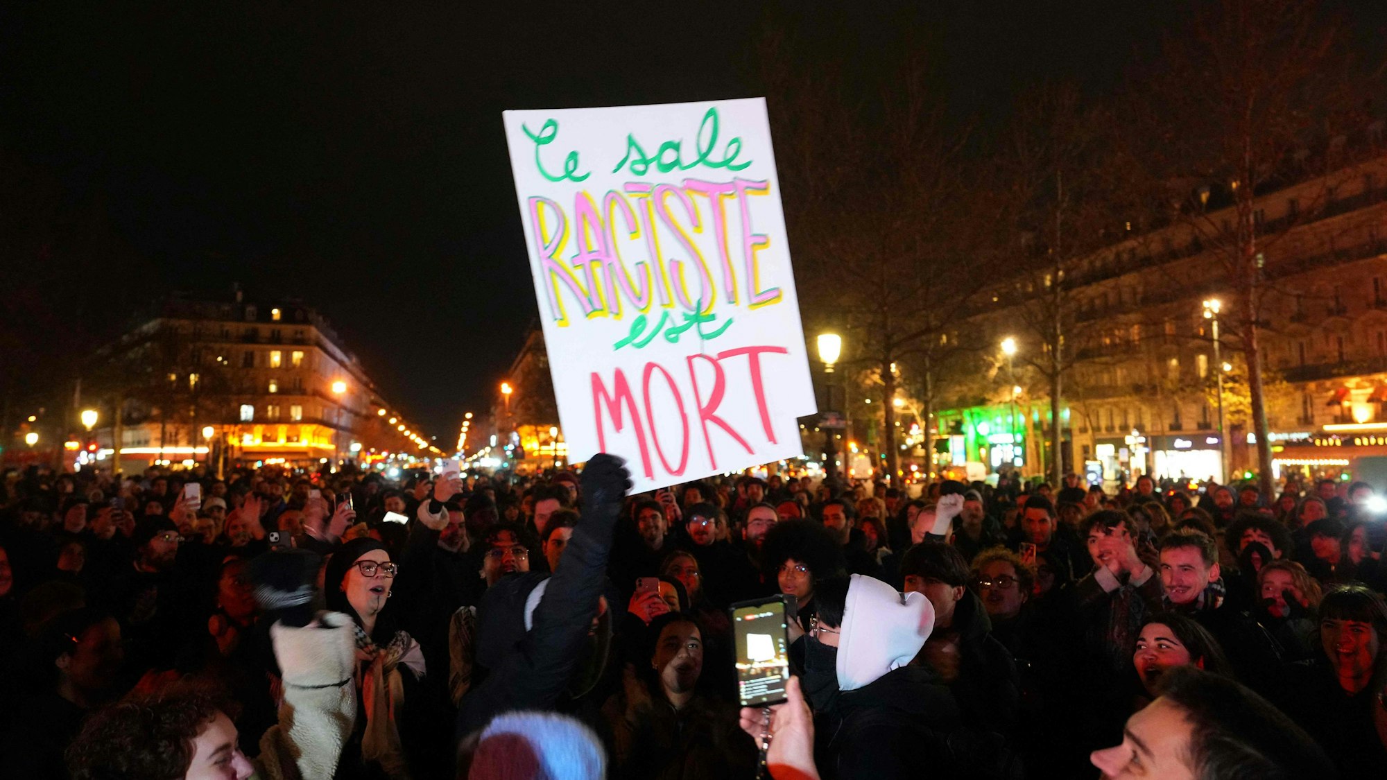 Ein Mann hält in Paris ein Plakat mit der Aufschrift ´Der dreckige Rassist ist tot` in die Höhe, während sich Menschen auf dem Place de la Republique versammeln, um an der Kundgebung ´Le Pen ist tot!» teilzunehmen, die von der Neuen Antikapitalistischen Partei (NPA) im Zentrum von Paris organisiert wurde, wenige Stunden nach dem Tod des französischen rechtsextremen Politikers Jean-Marie Le Pen.