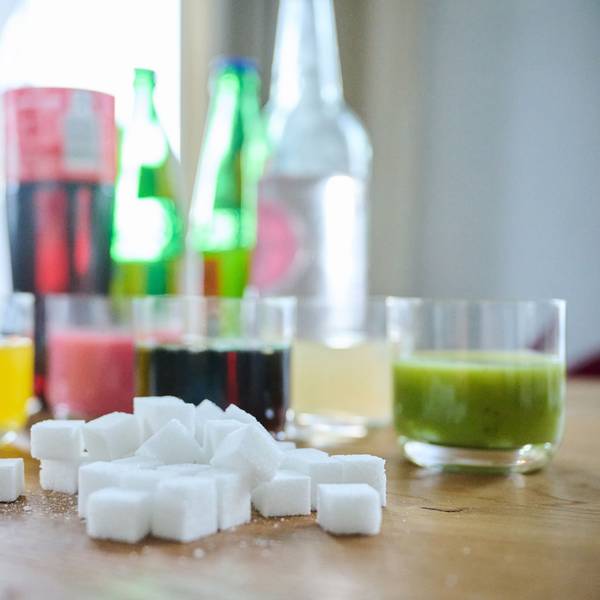 Fünf unterschiedliche Arten Softdrinks und die Flaschen dazu stehen zusammen mit Zuckerwürfel auf einem Tisch.