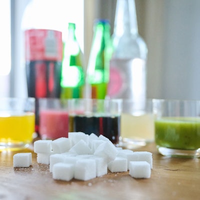 Fünf unterschiedliche Arten Softdrinks und die Flaschen dazu stehen zusammen mit Zuckerwürfel auf einem Tisch.