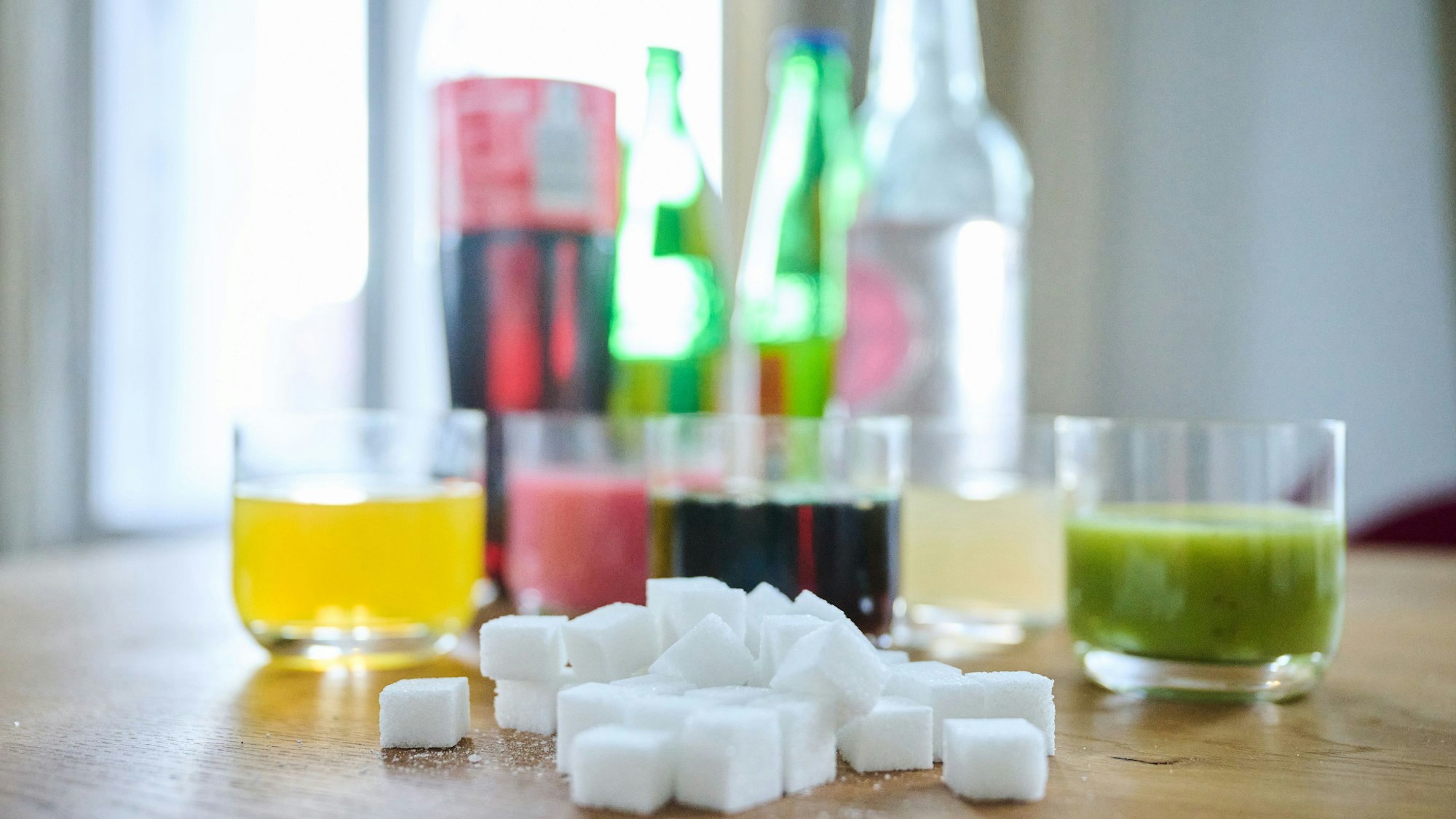 Fünf unterschiedliche Arten Softdrinks und die Flaschen dazu stehen zusammen mit Zuckerwürfel auf einem Tisch.