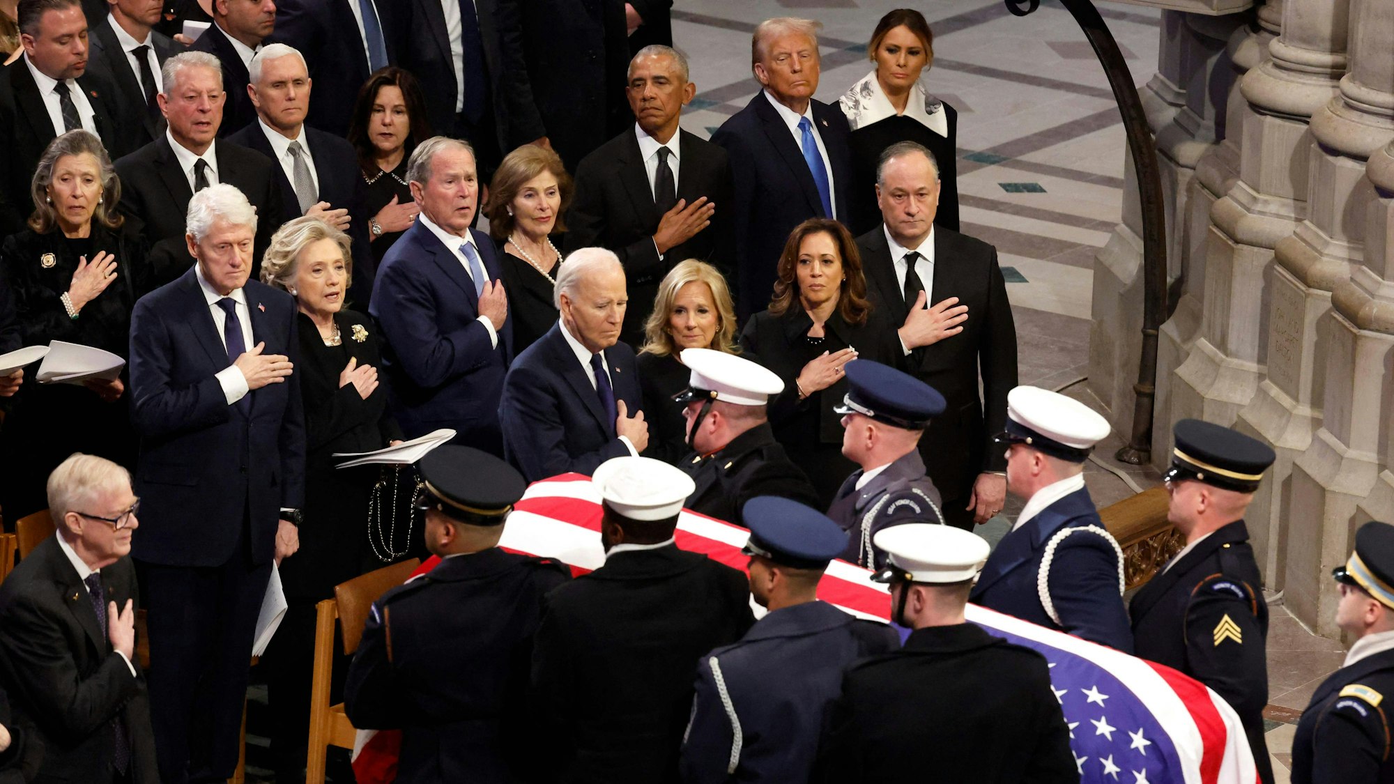 WASHINGTON, DC - JANUARY 09: U.S. Military Body Bearers carry the flag-draped casket bearing the remains of former U.S. President Jimmy Carter from the Washington National Cathedral following his state funeral as (L-R) Jack Carter, Former U.S. Vice Presidents Al Gore and Mike Pence, Karen Pence, former U.S. President Bill Clinton, former Secretary of State Hillary Clinton, former U.S. President George W. Bush, Laura Bush, former U.S. President Barack Obama, U.S. President-elect Donald Trump, Melania Trump, U.S. President Joe Biden, first lady Jill Biden U.S. Vice President Kamala Harris and second gentleman Doug Emhoff look on on January 09, 2025 in Washington, DC. President Joe Biden declared today a national day of mourning for Carter, the 39th President of the United States, who died at the age of 100 on December 29, 2024 at his home in Plains, Georgia. Chip Somodevilla/Getty Images/AFP (Photo by CHIP SOMODEVILLA / GETTY IMAGES NORTH AMERICA / Getty Images via AFP)