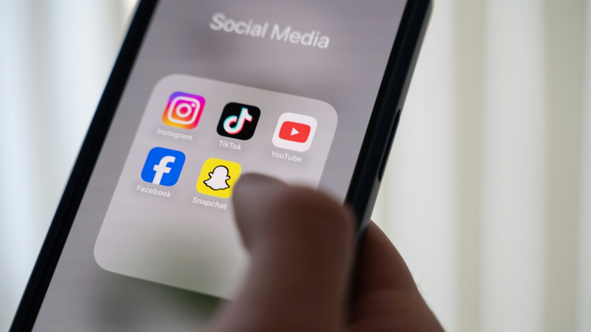 Eine Person hält ein Smartphone, auf dessen Display verschiedene Social Media Apps angezeigt werden.