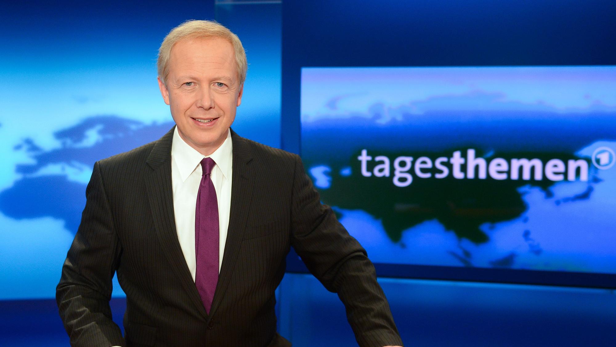 Tim Buhrow steht im Studio der Tagesthemen. Er trägt einen schwarzen Anzug und ein weißes Hemd.
