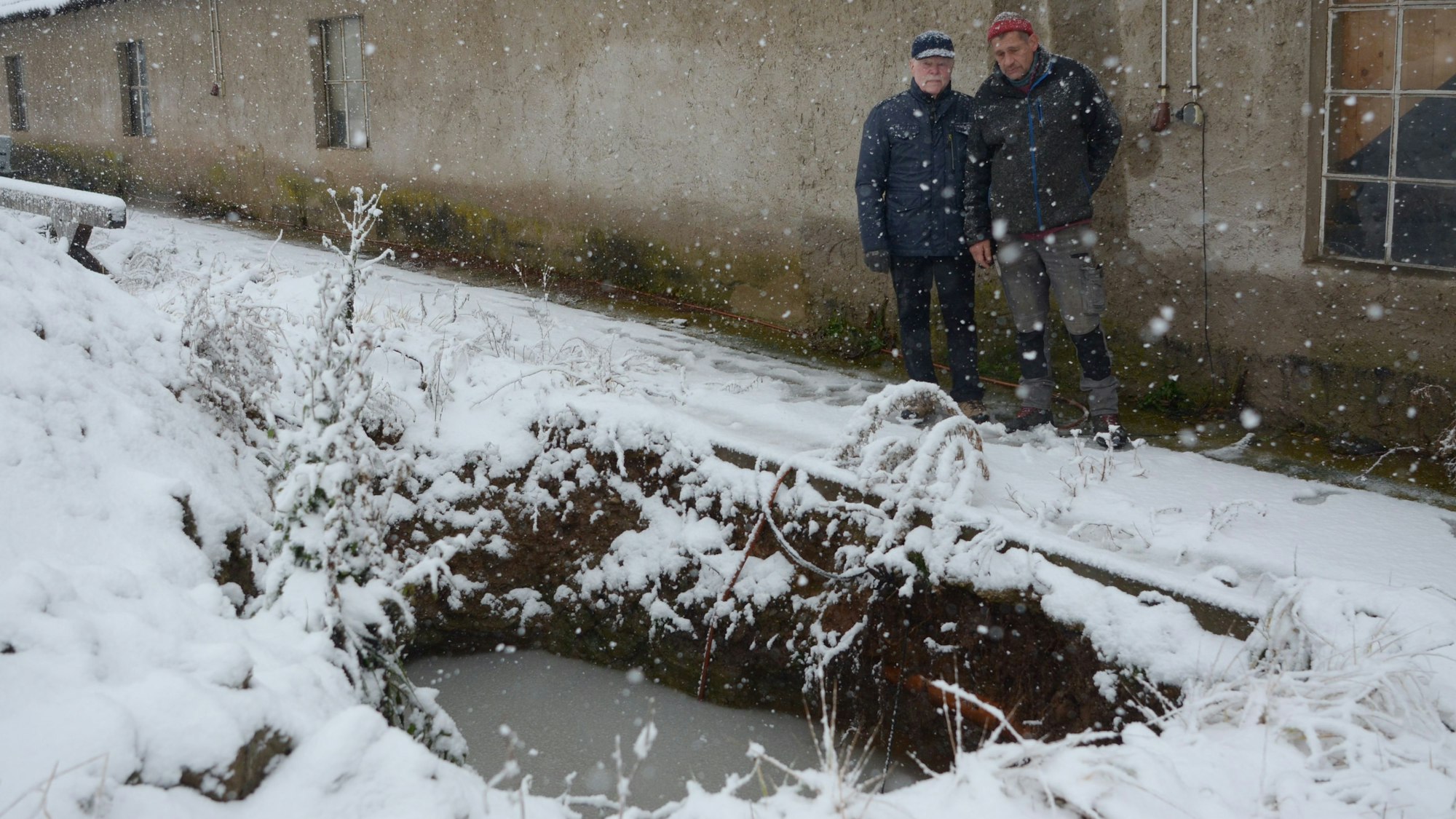 Zwei Männer stehen vor einer zur Hälfte mit Wasser gefüllten Grube.
