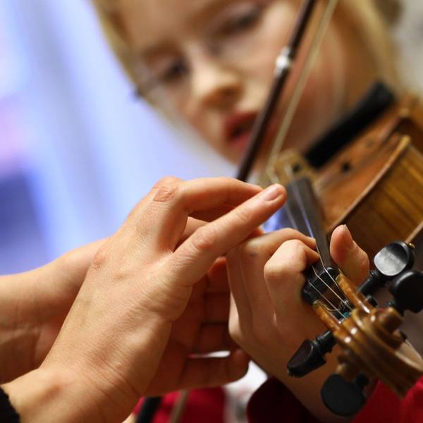 Die Hand der einer elfjährigen Musikschülerin von der Musiklehrerin beim Geigespiel korrigiert.