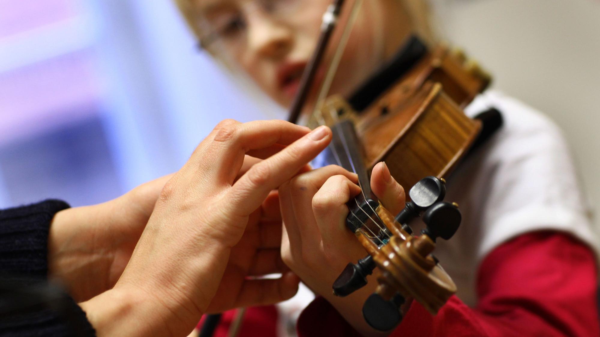 Die Hand der einer elfjährigen Musikschülerin von der Musiklehrerin beim Geigespiel korrigiert.