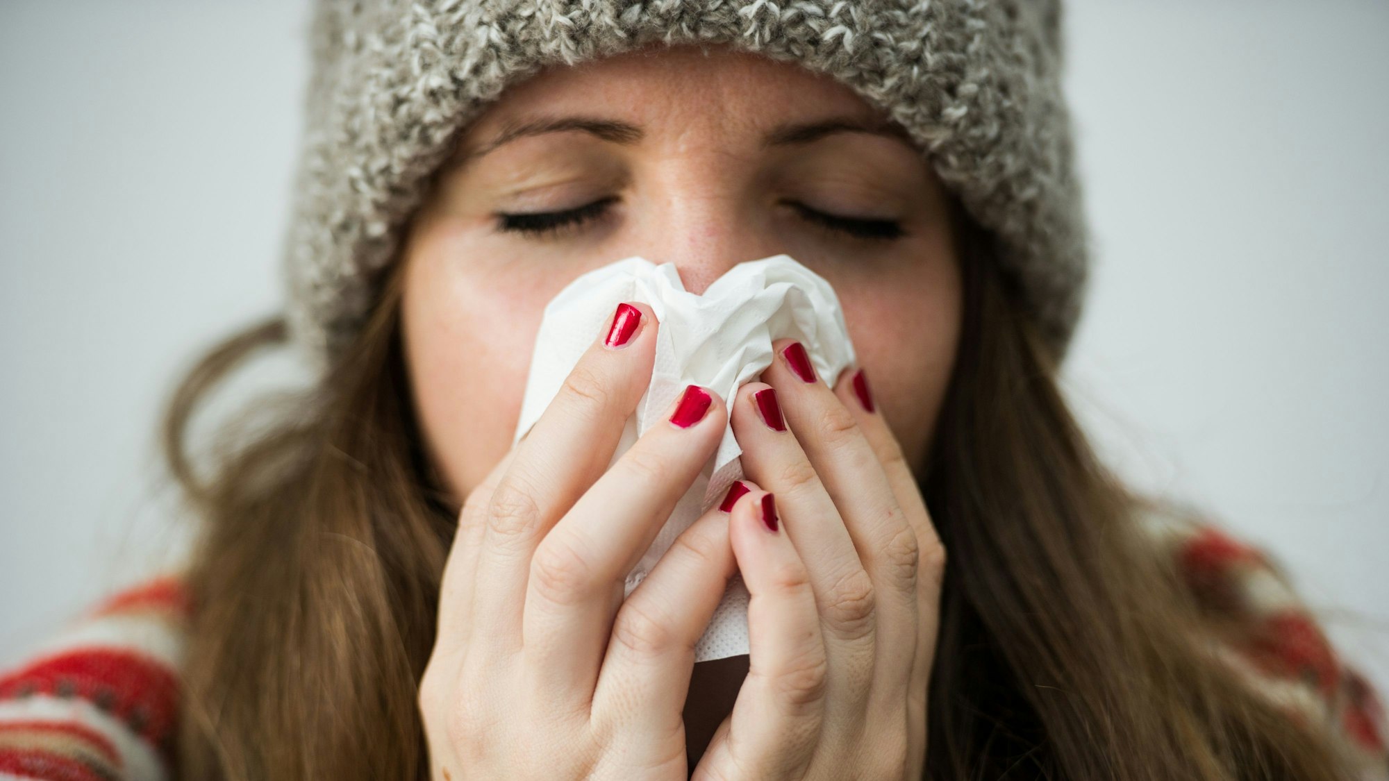 Eine junge Frau hält sich ein Taschentuch vor das Gesicht.