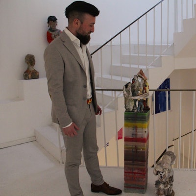Ein Mann steht auf einem Treppenabsatz, neben ihm steht ein Kunstobjekt.