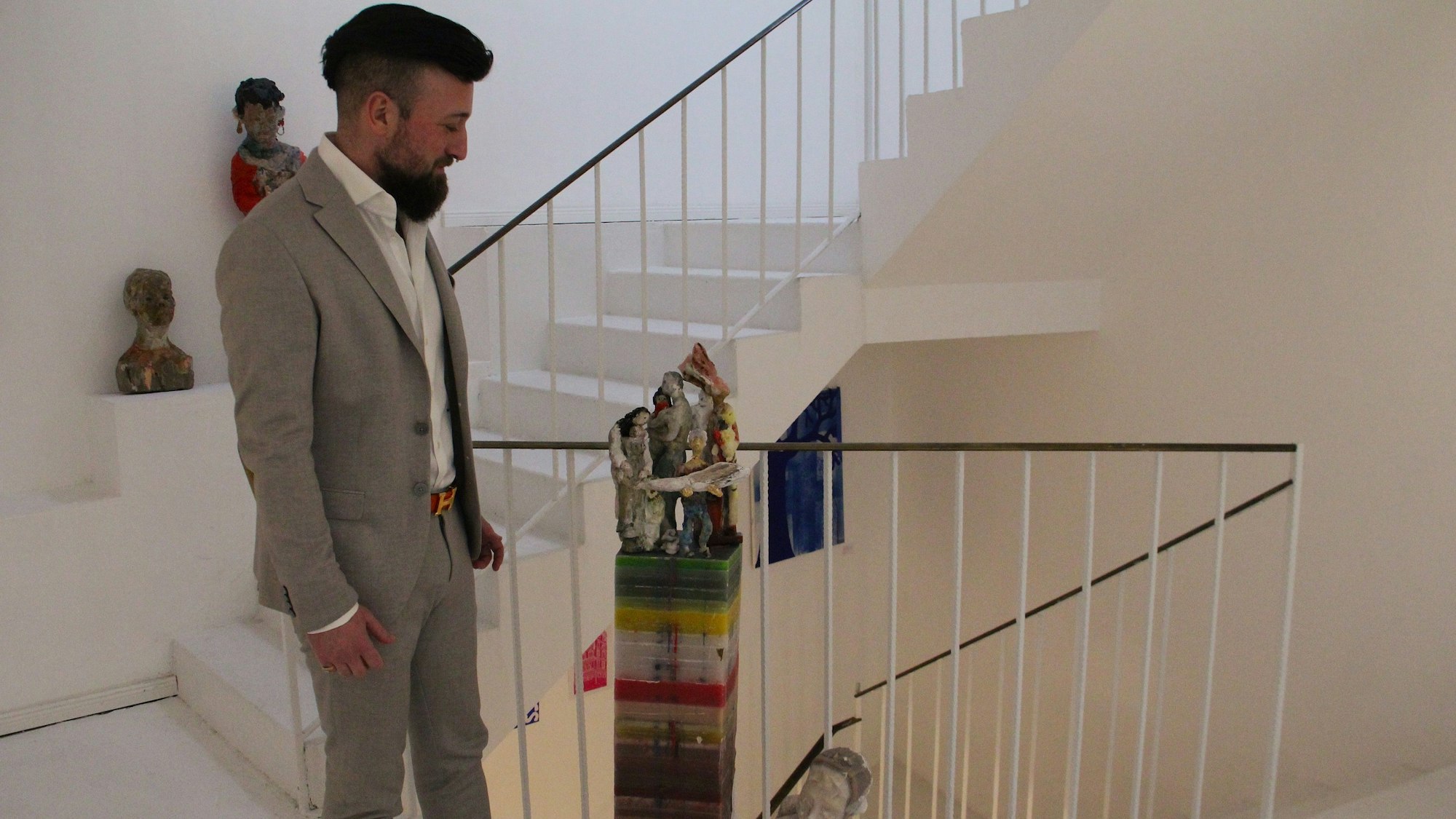 Ein Mann steht auf einem Treppenabsatz, neben ihm steht ein Kunstobjekt.