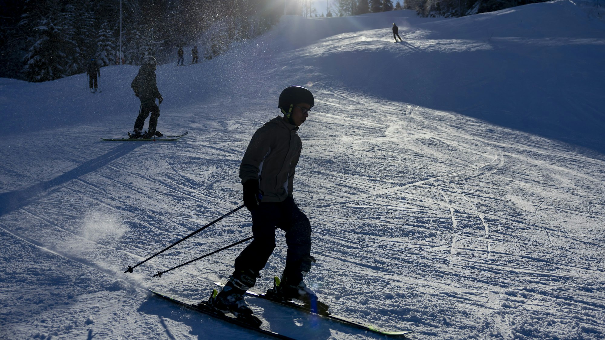 Personen fahren auf Skiern und dem Snowboard eine Piste hinab.