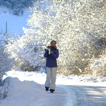 Eine Spaziergängerin im verschneiten Urfttal hat ihre Langlaufskier geschultert.