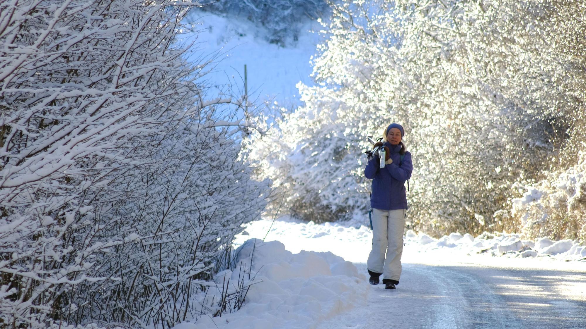 Das Archivfoto zeigt eine Spaziergängerin im verschneiten Urfttal, die ihre Langlaufskier geschultert hat.