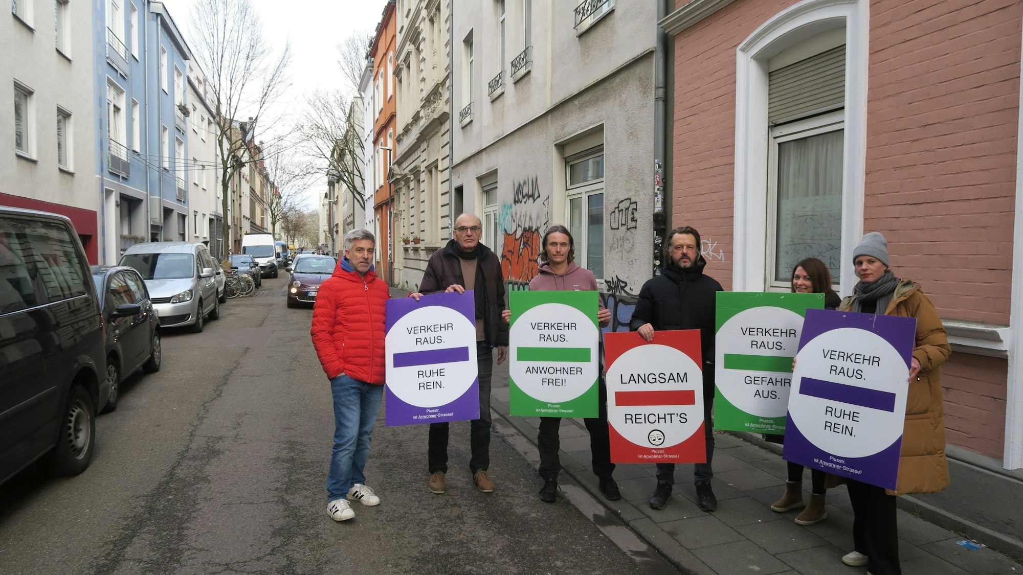 Sechs Menschen stehen mit Transparenten auf einer schmalen Straße.
