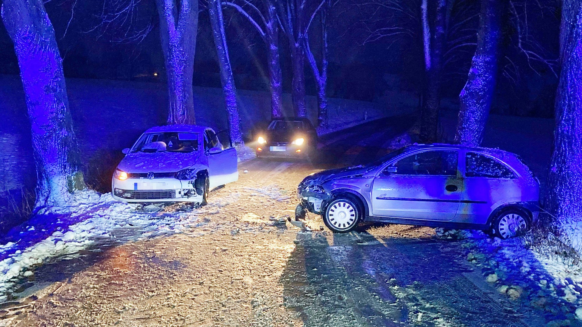 Zwei Autos stehen nach einem Unfall auf einer schneeglatten Allee zwischen den Alleebäumen.