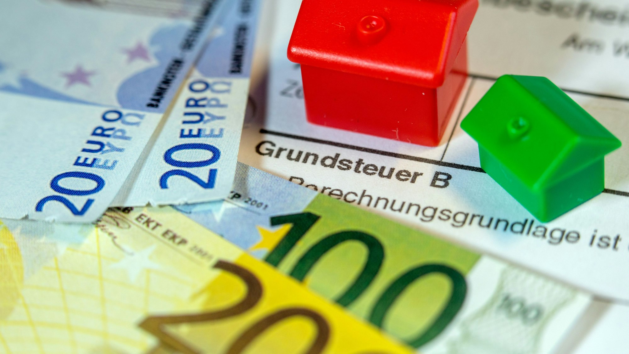 Ein Spielzeughaus und die Nachbildung von Euro-Geldscheinen liegen auf einem Abgabenbescheid für die Entrichtung der Grundsteuer.