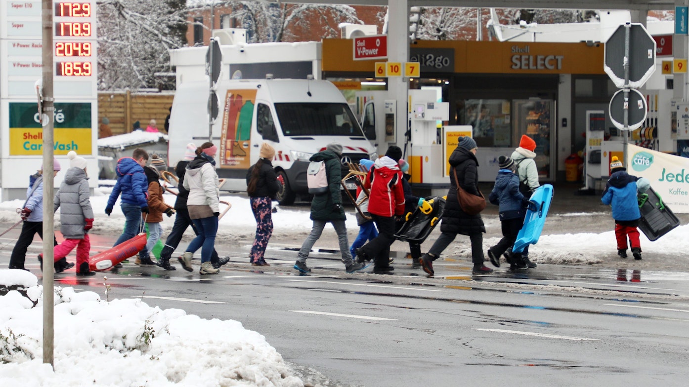 Kinder gehen mit Rodel und Schlitten über eine Straße in Bergisch Gladbach-Moitzfeld.