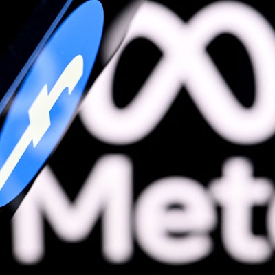 Ein Smartphone mit einem Facebook-Logo auf dem Bildschirm wird vor einen unscharfen Hintergrund mit Meta-Logo gehalten.