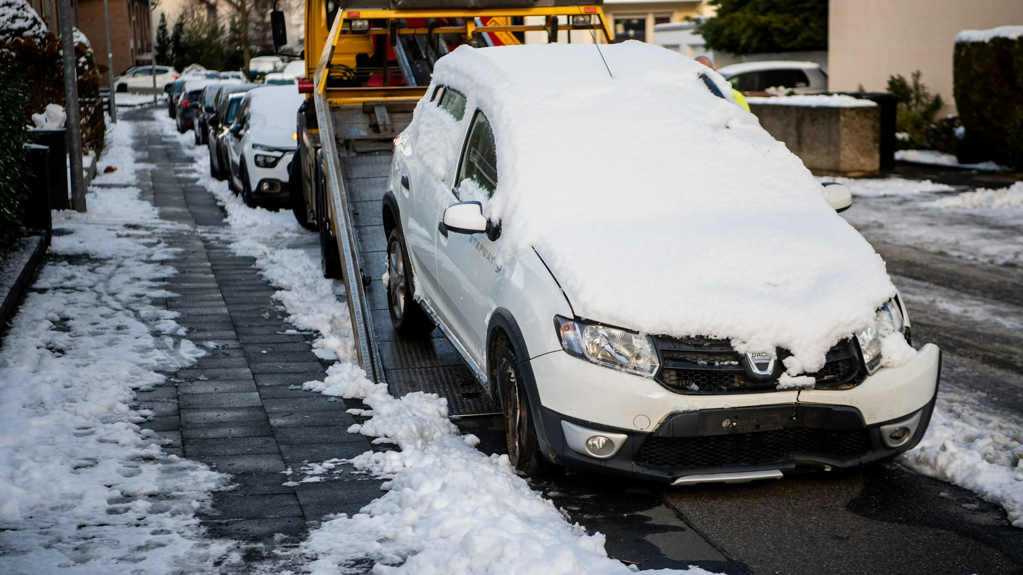 Das Bild zeigt ein schneebedecktes Auto, das auf einen Abschlepp-Lkw gezogen wird.