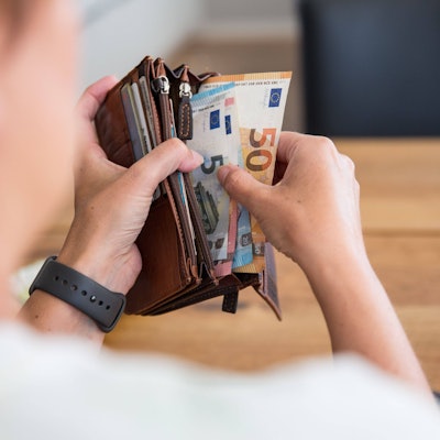 Eine Person hält eine Geldbörse mit Bargeld in den Händen. Die Geldscheine haben die Währung Euro und sind von unterschiedlichem Geldwert.