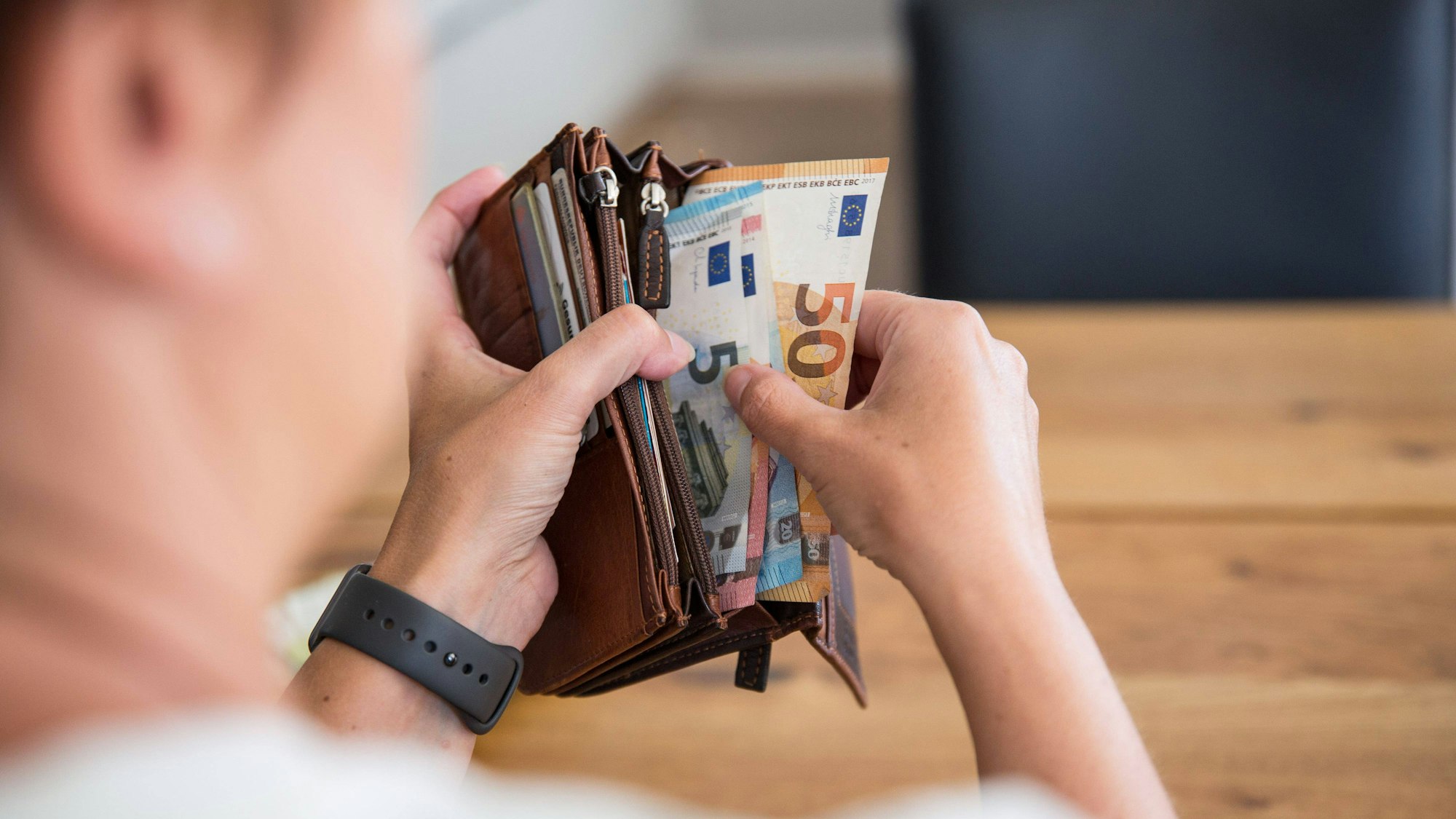 Eine Person hält eine Geldbörse mit Bargeld in den Händen. Die Geldscheine haben die Währung Euro und sind von unterschiedlichem Geldwert.