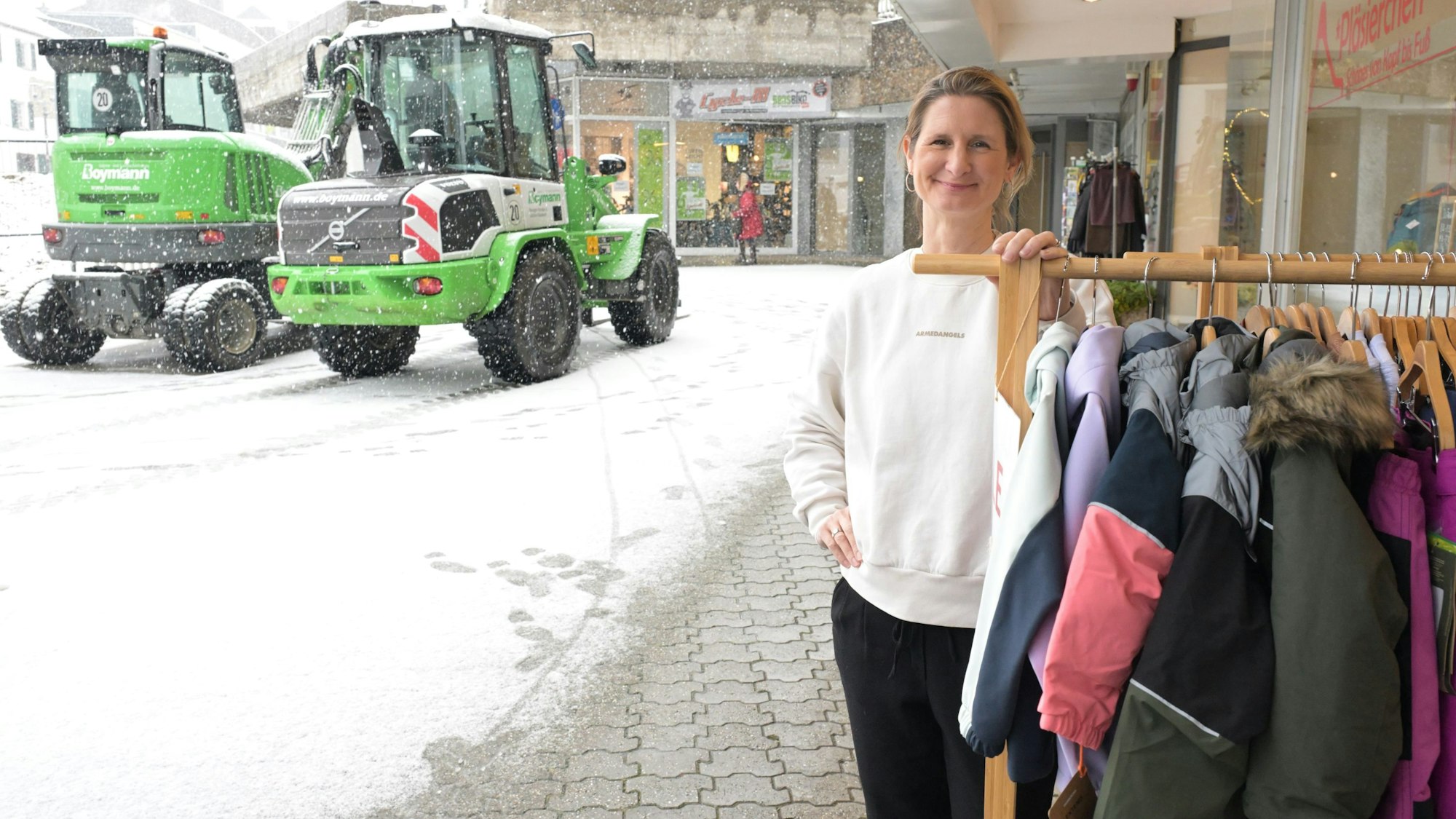 Die Geschäftsfrau steht vor ihrem Geschäft neben einem Ständer mit Jacken.