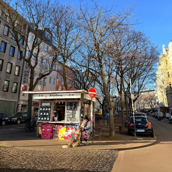 Eine Frau und ihr Hund sitzen vor dem King Georg Büdchen.