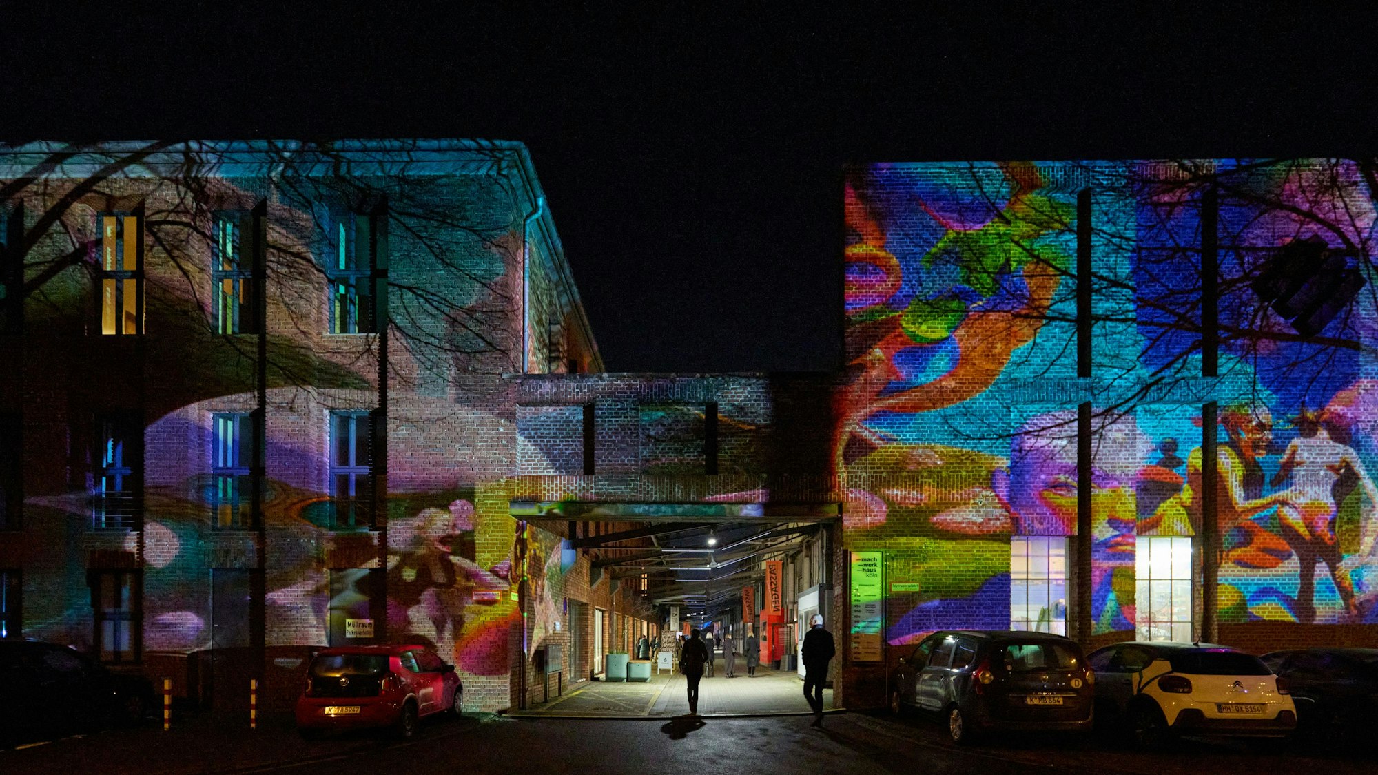 An der großen Backsteinwand des ehemaligen KHD-Gebäudes in Kalk küssen sich Menschen, bewegen sich Muster, wehen Äste im Wind.
