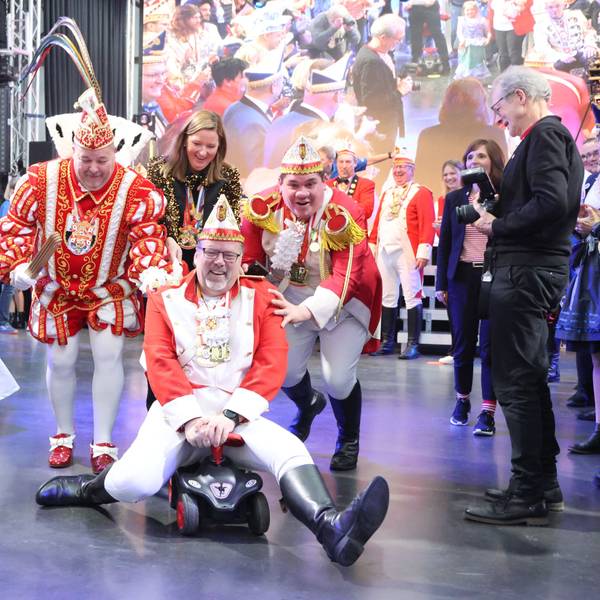 Ein Mann einer Karnevalsgesellschaft fährt mit einem Bobbycar durch die Menschenmenge.