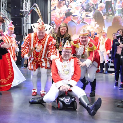 Ein Mann einer Karnevalsgesellschaft fährt mit einem Bobbycar durch die Menschenmenge.