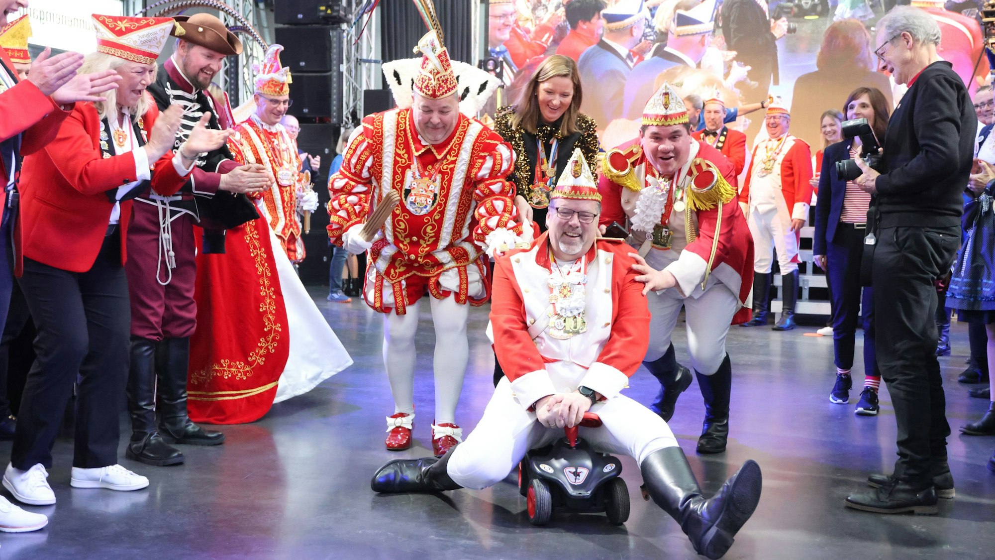 Ein Mann einer Karnevalsgesellschaft fährt mit einem Bobbycar durch die Menschenmenge.