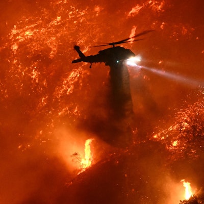 A fire fighting helicopter drops water as the Palisades fire grows near the Mandeville Canyon neighborhood and Encino, California, on January 11, 2025. The Palisades Fire, the largest of the Los Angeles fires, spread toward previously untouched neighborhoods January 11, forcing new evacuations and dimming hopes that the disaster was coming under control. Across the city, at least 11 people have died as multiple fires have ripped through residential areas since January 7, razing thousands of homes in destruction that US President Joe Biden likened to a "war scene." (Photo by Patrick T. Fallon / AFP)