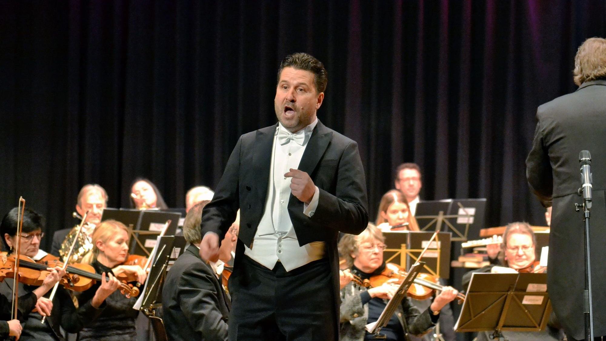 Das Foto zeigt den Solisten Daniel Szeili. Im Hintergrund ist das Orchester zu sehen.