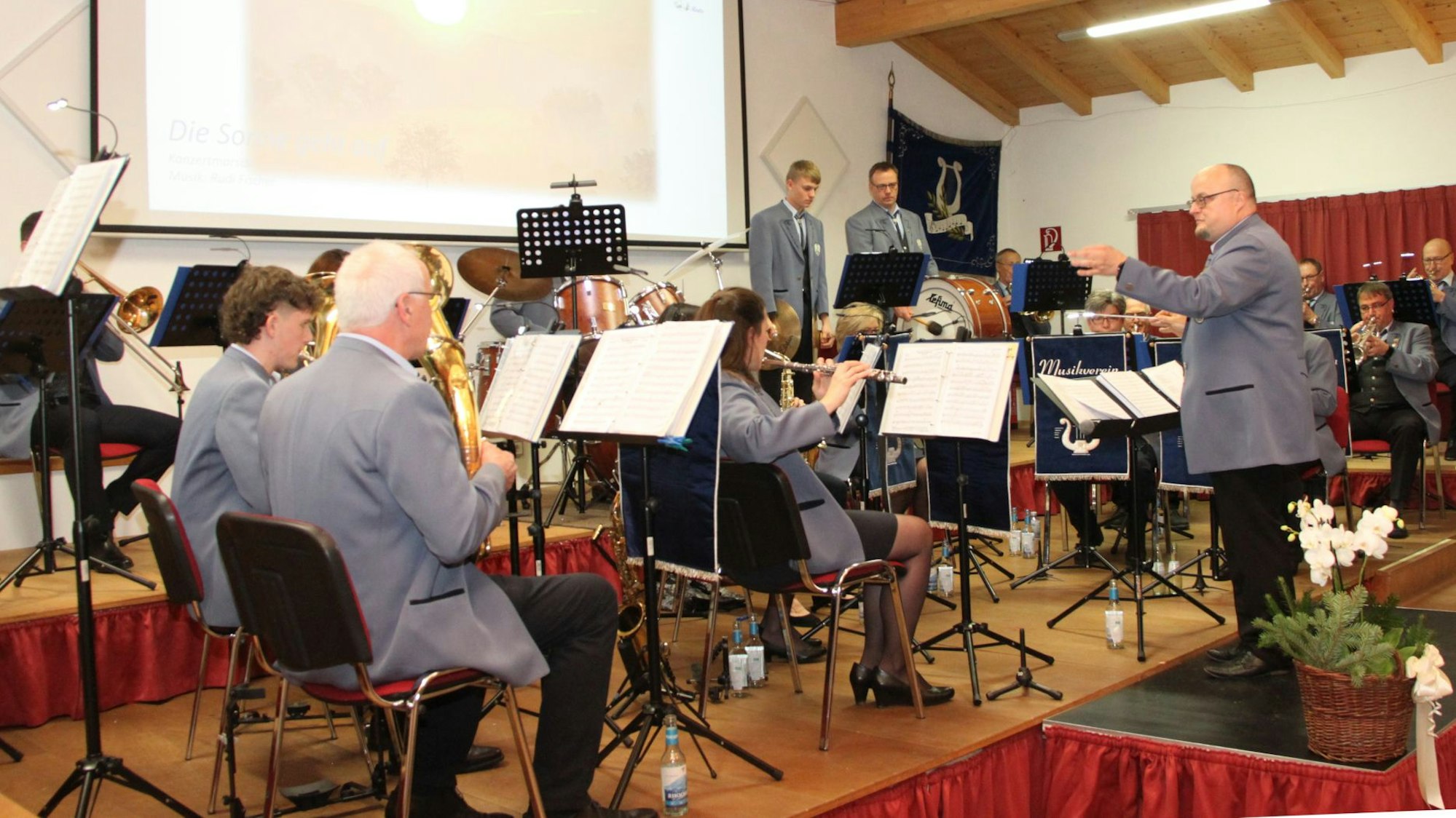 Die Mitglieder sitzen auf der Bühne und musizieren, Jörg Schramm steht davor und dirigiert.