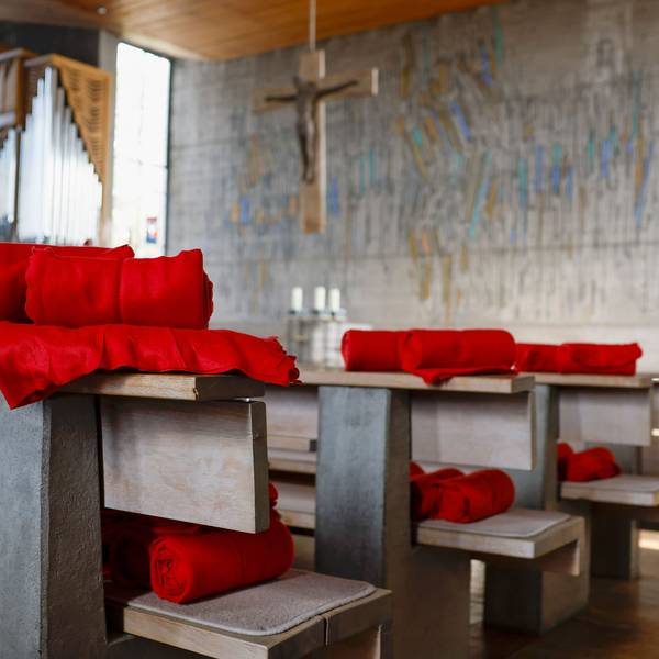 In einer Kirche liegen rote Decken auf den Bänken für die Gläubigen bereit.