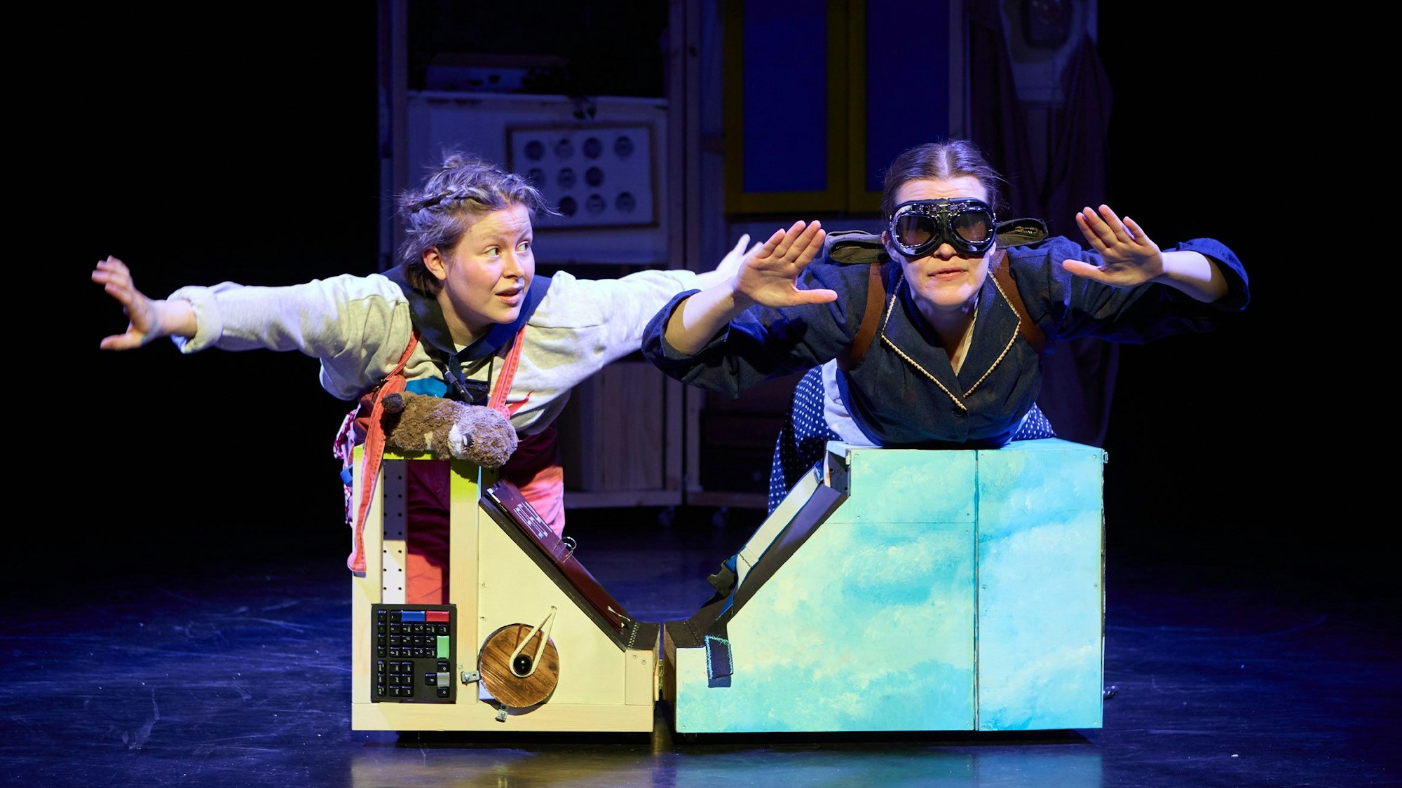 Zwei Schauspielerinnen liegen auf einem an einen Schrank erinnernden Objekt auf der Bühne.