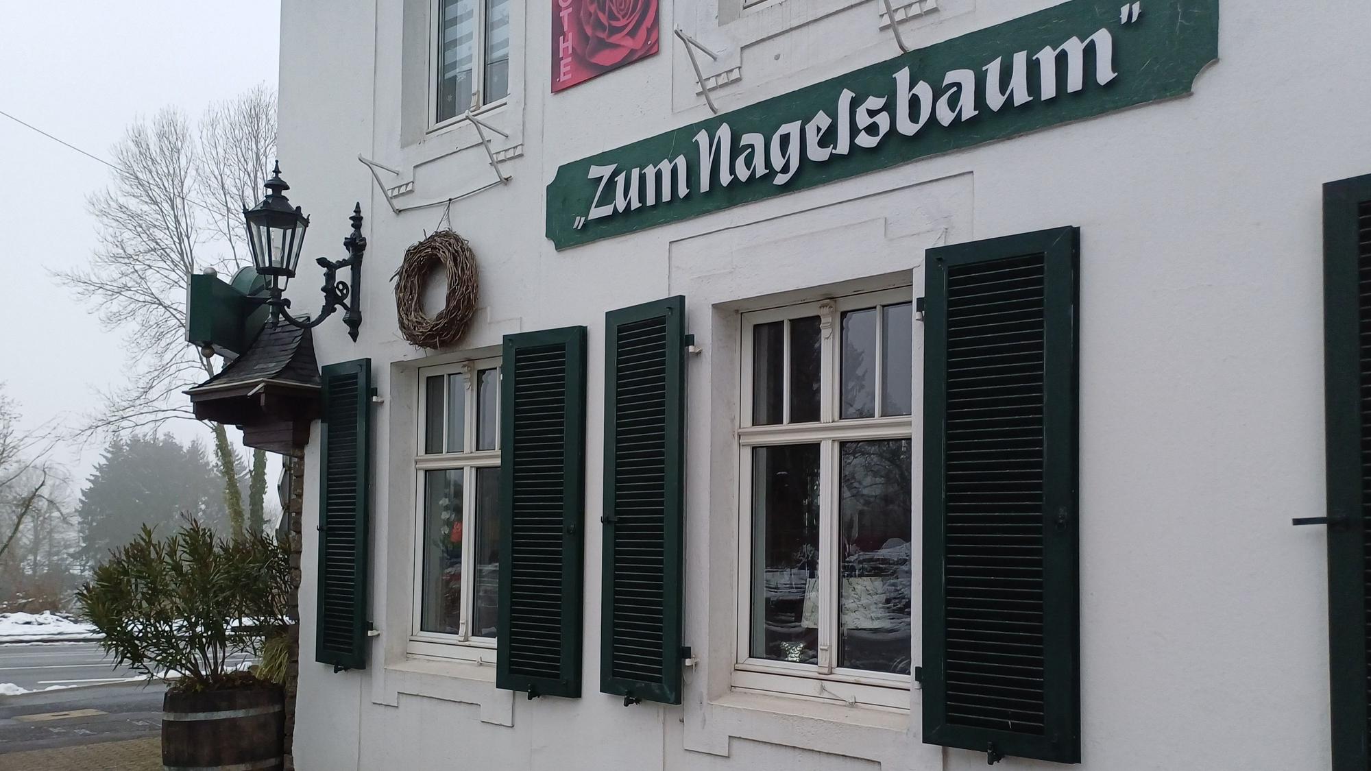 Ein Schild mit der Aufschrift „Zum Nagelsbaum“ hängt an einem Haus.