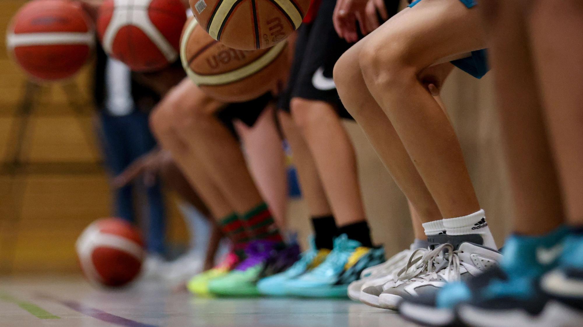 Beine von Kindern und Jugendlichen, die in einer Sporthalle Basketbälle prellen.