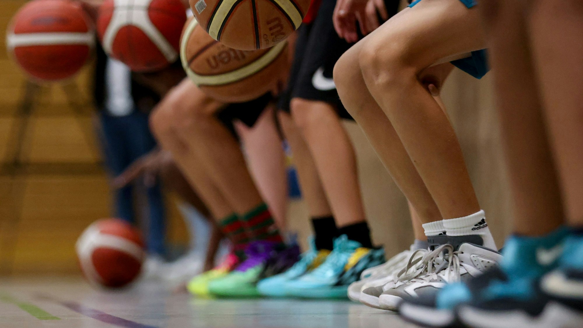 Beine von Kindern und Jugendlichen, die in einer Sporthalle Basketbälle prellen.