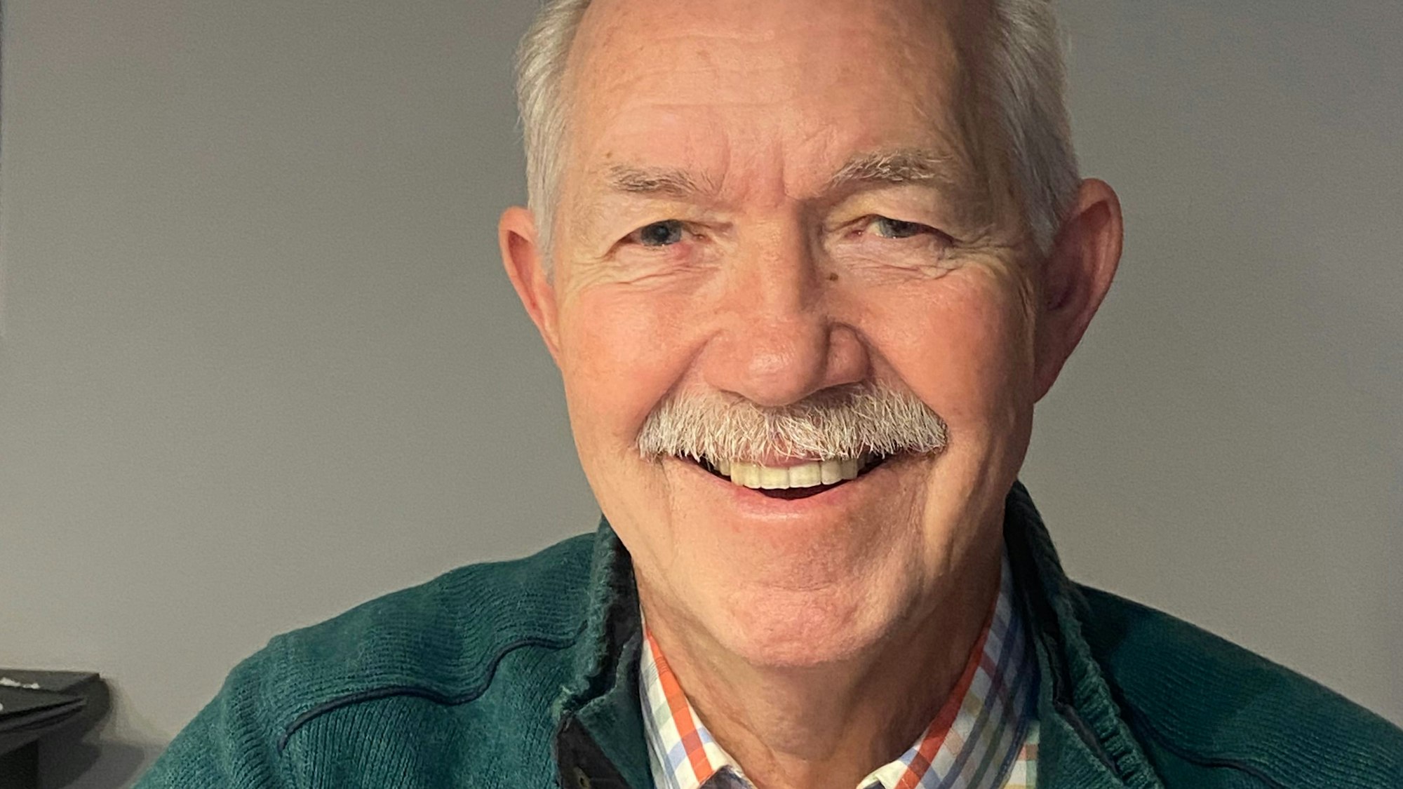 Ein Mann mit grauem Haar und grauem Schnäuzer lacht in die Kamera.