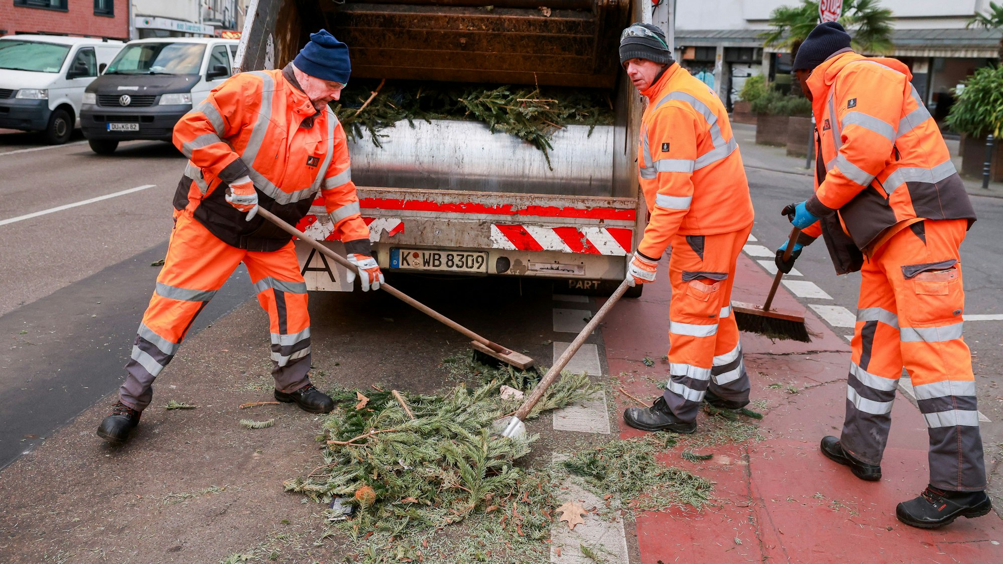 Drei Mülllader kehren Reste des Tannenmülls ein.