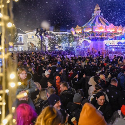 Zahlreiche Menschen stehen in einem Freizeitpark vor einem großen Karussell.