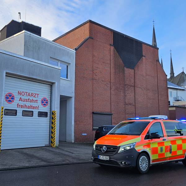 Zu sehen ist das Krankenhaus in Bedburg, im Vordergrund das Fahrzeug des Notarztes im Einsatz mit Blaulicht.