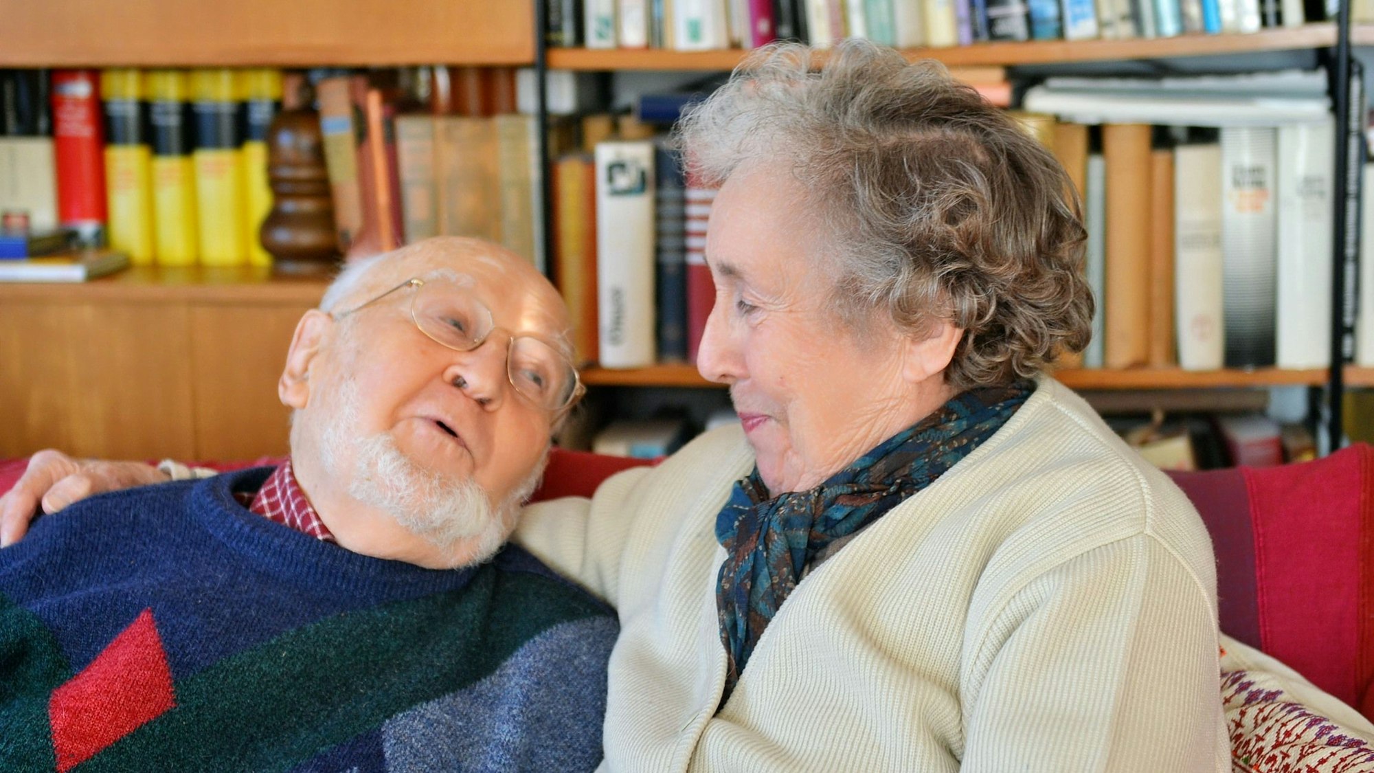 Jacqueline und Hubertus Dobers sitzen nebeneinander auf ihrem Sofa. Sie hat den Arm um ihn gelegt.