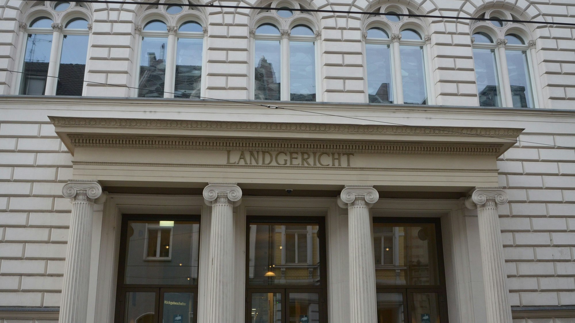 Das Foto zeigt den Eingang des Landgerichts, ein helles Gebäude mit Rundbogenfenstern und Säulen vor der Tür.