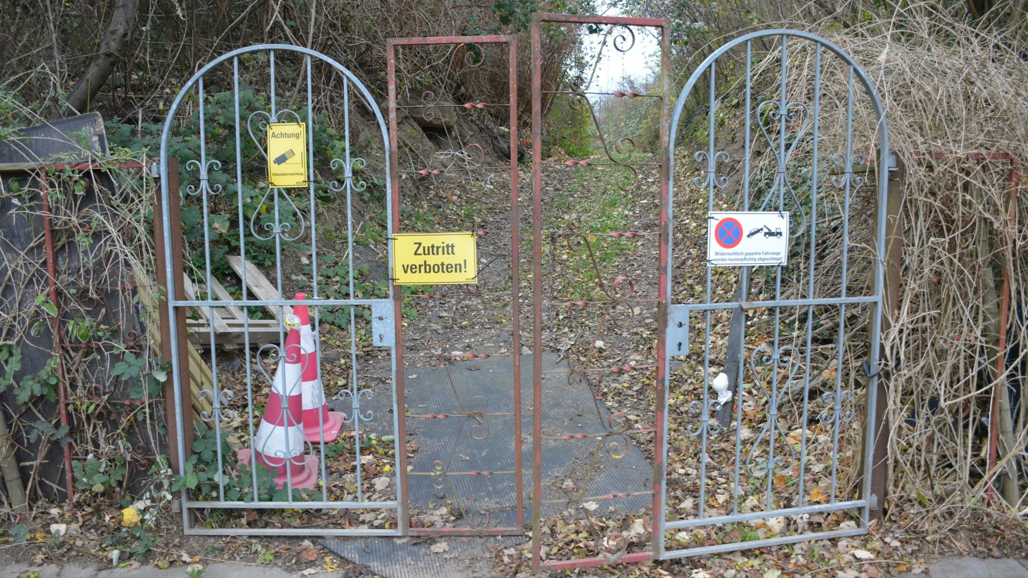 Hinter altersschwachen Toren führe ein Weg auf eine Brachgelände.